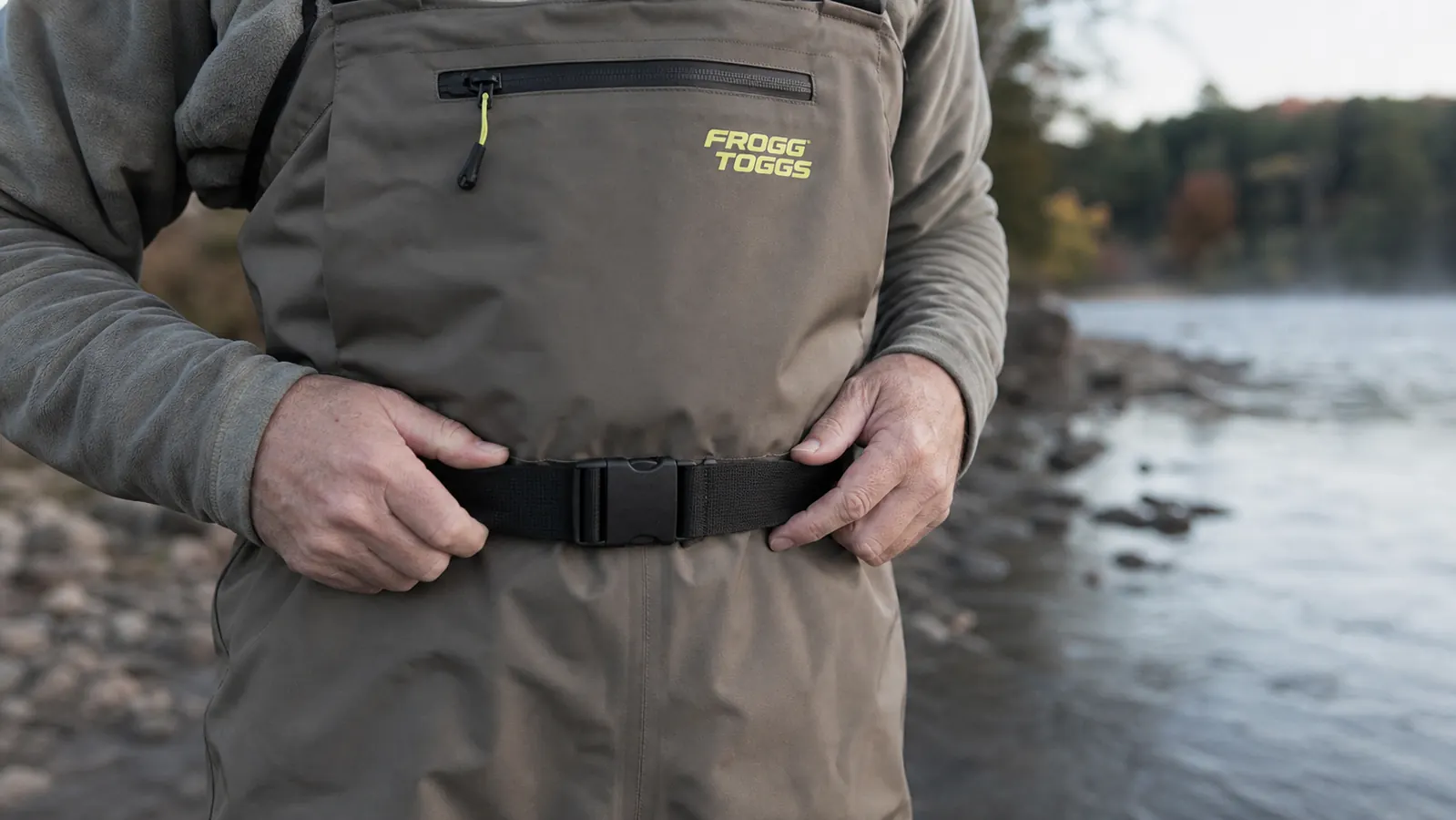 Close-up of Frogg Toggs Hellbender chest waders with a wading belt cinched at the waist before entering the river