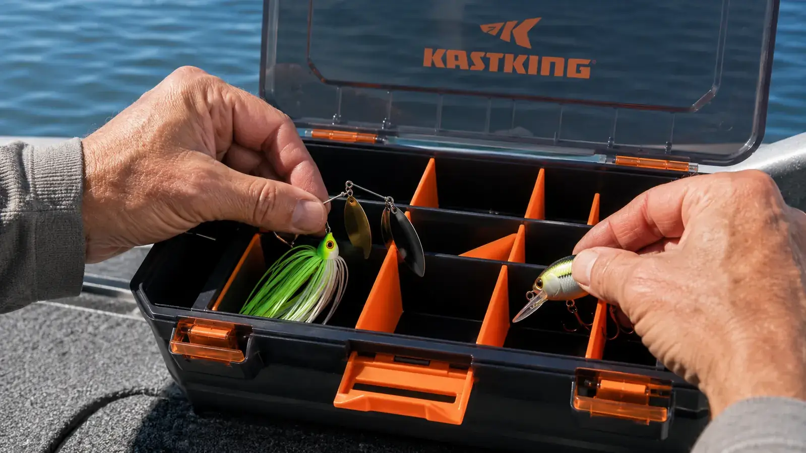 Hands sorting a spinnerbait and crankbait into the deeper compartments of an open KastKing tackle tray